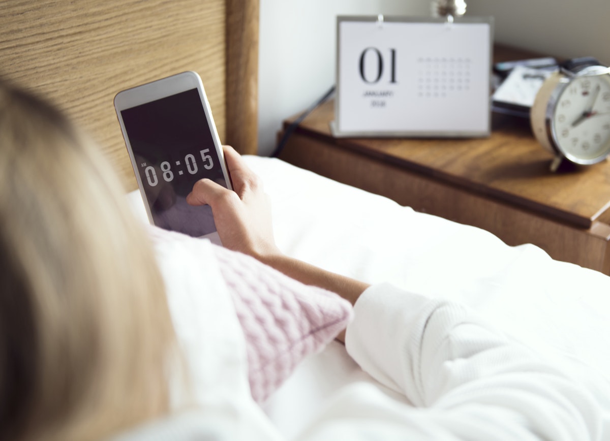 woman on mobile device checking the time with calendar and alarm clock